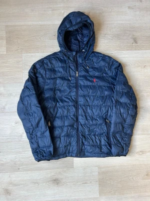 Blå Ralph Lauren Lätt Dunjacka Storlek XL - Fin RL vårjacka i blå färg. Jackan är i mycket bra skick och sparsamt använd. |  Äkta som allt annat jag säljer! ✅ |  Storlek: XL | Skick: Mycket Bra Skick - (Se sista bild) ett litet hål som är tejpat på armen | Färg: Blå | Märke: Ralph Lauren | Modell: Jacka |  Hör gärna av dig vid frågor så svarar jag så fort jag kan! 😁|   (SKU - 83)