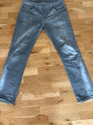 Grå jeans från Levi's - Säljer ett par grå jeans från Levi's med klassisk femficksdesign och raka ben. Jeansen har en snygg tvättad look och är tillverkade i bomull. Perfekta för dig som gillar en avslappnad och stilren stil.
