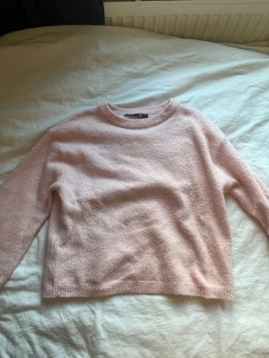 Ljusrosa stickad tröja 157 - Mysig ljusrosa stickad tröja från Lager 157 med rund halsringning och långa ärmar. Tröjan har en enkel, rak passform och ribbade muddar vid ärmslut och nederkant.