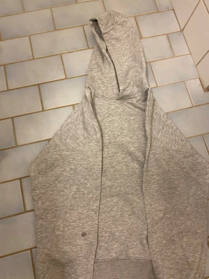 Ljusgrå hoodie med dragkedja - En enkel och stilren ljusgrå hoodie med dragkedja framtill och huva. Tillverkad i mjukt sweatshirtmaterial, perfekt för en avslappnad look. Hoodien har långa ärmar och ribbade muddar vid ärmslut och nederkant.