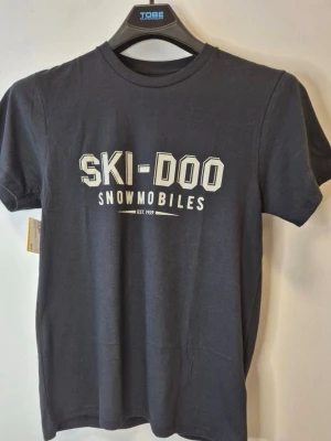 Svart Ski-Doo t-shirt - Snygg svart t-shirt från Ski-Doo med vit text 'SKI-DOO SNOWMOBILES' tryckt på bröstet. Klassisk rund halsringning och korta ärmar. Perfekt för dig som gillar enkel och stilren design.