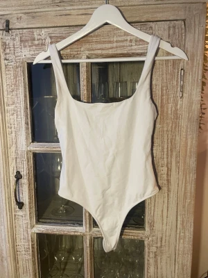 Vit body med djup rygg från Zara - Säljer en enkel och stilren vit body med breda axelband och rundad urringning både fram och bak. Bodyn har en klassisk, tight passform och är tillverkad i ett mjukt stretchigt material som sitter skönt mot kroppen. Storlek 38 men mer som 34/36 eller XS/S. Liten fläck i armhålan.