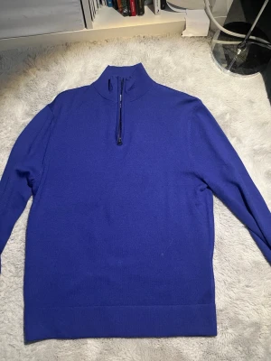 Blå merinoulltröja med halv dragkedja - Snygg blå stickad tröja från These Glory Days i mjuk superior merinoull. Tröjan har hög krage och halv dragkedja framtill, perfekt för lager på lager och en clean look. Långa ärmar och ribbade muddar ger en stilren finish.