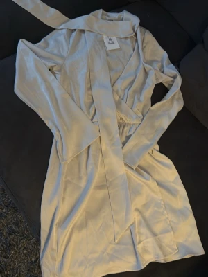 Beige satin klänning från Bik Bok - Stilren beige klänning i satinmaterial med lång ärm . Enkel och elegant design. Helt ny storlek S 