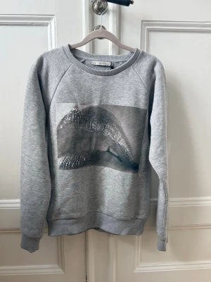 Grå sweatshirt med tryck  - Snygg grå sweatshirt från Gestuz med ett snyggt på framsidan. Tröjan har rund halsringning, långa ärmar och ribbade muddar vid ärmslut och nederkant. Perfekt för en avslappnad och trendig look.