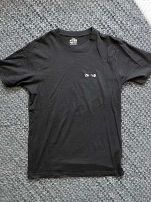 Handbroderad Svart t-shirt från Denim Project - Svart t-shirt från Denim Project. På bröstet finns en liten ljusblå broderad text 'JOH 14:6'. "Filippus sade till honom: 'Herre, visa oss Fadern, så räcker det för oss.”