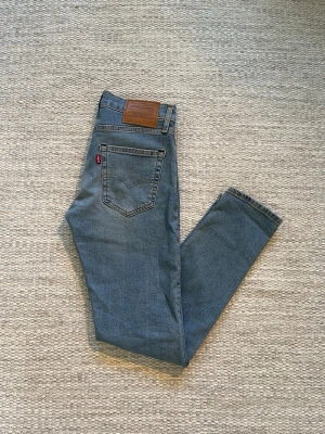 Levi's blå raka jeans - Klassiska blå jeans från Levi's med rak passform och fem fickor. Jeansen har en ljus tvätt och den ikoniska röda Levi's-lappen på bakfickan samt läderpatch i midjan. Tillverkade i slitstark denim, perfekta för en avslappnad och trendig look.