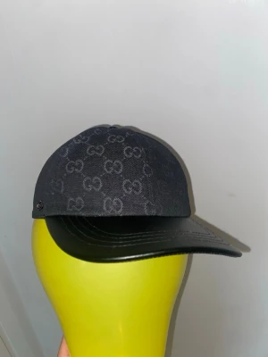 Svart gucci keps - Snygg svart keps från Gucci med klassiskt GG-monogram över hela ovandelen och böjd skärm i svart läder. Perfekt accessoar för dig som gillar exklusiv streetstyle och vill sticka ut med en lyxig touch.