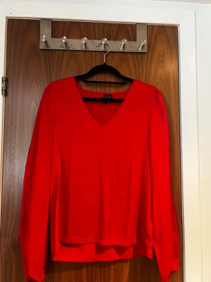 Röd v-ringad blus från Vero Moda  - Snygg röd blus från Vero Moda med v-ringning och långa ärmar. Blusen har en avslappnad passform och är tillverkad i ett lätt, mjukt tyg som ger ett fint fall. Perfekt att styla med jeans eller kjol för en trendig look.
