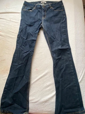 Mörkblå bootcut jeans - Säljer ett par mörkblå bootcut jeans med klassisk femficksdesign och kontrastsömmar. Jeansen har normal midja och utsvängda ben. Perfekta för dig som gillar en retroinspirerad look och vill ha ett par bekväma jeans i tidlös modell.