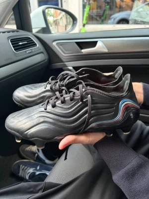 Svarta Adidas Copa fotbollsskor - Säljer ett par svarta Adidas Copa fotbollsskor med klassisk design och vågiga detaljer på sidan. Skorna har vita och röda detaljer samt dobbar för spel på gräs. Tillverkade i syntetmaterial med snörning för bra passform. Det är elite modellen så dom kostar 2400kr i nypris ungefär och dom är endast använda en match, nackdelen är att jag har klippt av snörena lite för att dom var svin långa. 