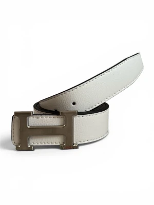 Vitt skärp med H-spänne i skinn - Snyggt vitt skärp i skinn med ett stort, silverfärgat H-format spänne. Bältet har en stilren och modern look med svarta kanter och diskreta sömmar. Perfekt accessoar för att lyfta din outfit.