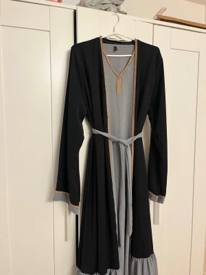 Två set abaya - Väldigt fin två set abaya med en ärmlös underklänning och en abaya till och matchande bälte. I strl L. Använd och slitaget syns på bilderna, bla på kopparfärgade bandet.