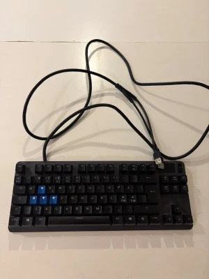SteelSeries kompakt tangentbord USB - Säljer ett kompakt svart tangentbord från SteelSeries med USB-anslutning. Tangentbordet har svarta tangenter med några blå piltangenter och en stilren design. Perfekt för gaming eller arbete vid datorn. Tillverkat i plast.