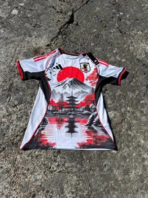 Japan Adidas fotbollströja med Mount Fuji - Japan special edition-tröja med riktigt unik design inspirerad av japansk kultur. Tröjan har Mount Fuji, tempel, röda körsbärsträd och klassiska japanska detaljer i svart, vitt och rött.  Skön passform och perfekt både för fotboll och som streetwear. Sticker definitivt ut jämfört med vanliga fotbollströjor. Priset är inte hugget i sten, så kom med bud!!