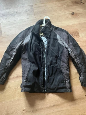 Svart racingjacka/motorcyckeljacka från Halvarssons - Snygg svart racingjacka/motorcyckeljacka från Halvarssons med grå detaljer och quiltat foder. Har inga skavanker och är sparsamt använd.