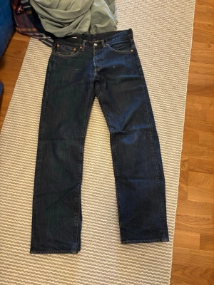 Mörkblå Levi's raka jeans - Säljer ett par klassiska mörkblå jeans från Levi's med rak passform. Jeansen har fem fickor, knappgylf och den ikoniska röda Levi's-lappen bak. Tillverkade i slitstark denim som ger en tidlös look.