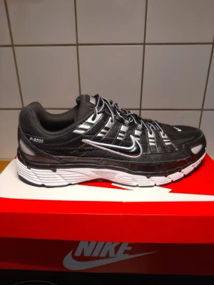 Nike P-6000 svart/vit sneaker använd 1 gång. - Nike P-6000 sneakers i svart och vitt med mesh och syntetiska paneler. Skon har en chunky vit sula, silverdetaljer och klassisk Swoosh-logga på sidan. Sportig design med snörning och vadderad häl för extra komfort. 