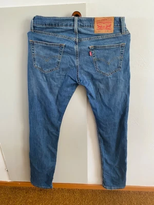 Blå Levi's jeans med raka ben - Klassiska blå jeans från Levi's med raka ben och fem fickor. Jeansen har en ljus tvätt och tydliga sömmar, samt den ikoniska läderlappen bak i midjan. Passar perfekt till en avslappnad stil och har en tidlös look.