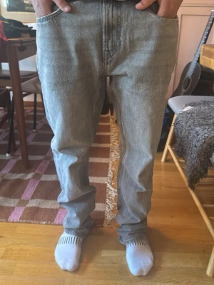 Ljusgrå raka lager 157 jeans - Säljer ett par ljusgrå jeans med rak passform och klassisk femficksdesign. Jeansen har en avslappnad look och är tillverkade i denim. Perfekta för dig som gillar en enkel och stilren stil.