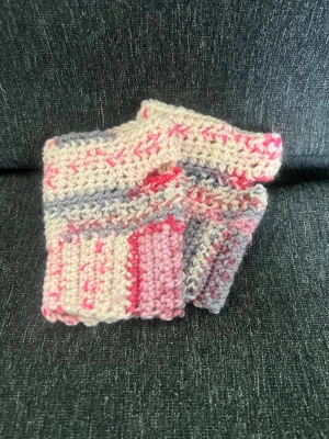 Virkade handledsvärmare i pastell - Ett par handgjorda virkade handledsvärmare i mjuka pastellfärger med inslag av rosa, grått och vitt. De har ett mysigt, chunky utseende. Perfekta för att hålla händerna varma och ändå ha fingrarna fria. Garnet är en blandning av Ull och akryl.