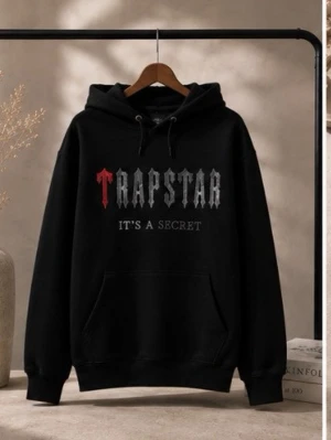 Svart Trapstar hoodie med tryck - Säljer en svart hoodie med huva och magficka. På bröstet står det 'Trapstar' i grå och röd text samt 'IT'S A SECRET' under. Hoodien har dragsko i huvan och ribbade muddar. Perfekt för dig som gillar streetwear och vill ha en stilren men ändå iögonfallande look.