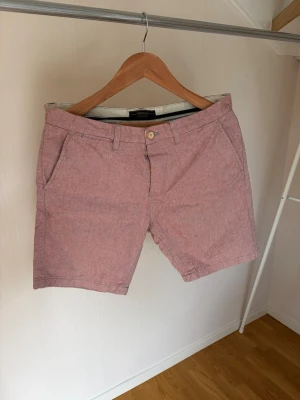 Ljusrosa bomullsshorts - Säljer ett par ljusrosa shorts i bomull med klassisk passform. Shortsen har två sidofickor fram, två bakfickor och bälteshällor. Perfekta för varma dagar och har en enkel knappstängning framtill.