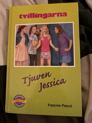 Tvillingarna: Tjuven Jessica - Tvillingarna: Tjuven Jessica av Francine Pascal är en ungdomsroman med hård pärm i grön färg. Omslaget har en färgglad illustration av fyra tjejer och boken ingår i serien Sweet Valley. Perfekt för dig som gillar spännande berättelser om vänskap och mysterier.