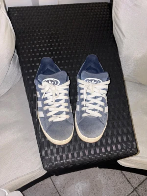  Adidas Originals sneakers 00s navy - Snygga blå Adidas Originals sneakers med klassiska vita ränder på sidorna och vit sula. Skorna har lågt skaft och är gjorda i mocka material med vita skosnören och Adidas-logga på plösen. Perfekta för en avslappnad streetstyle. Säljer då de knappt kommit till användning 