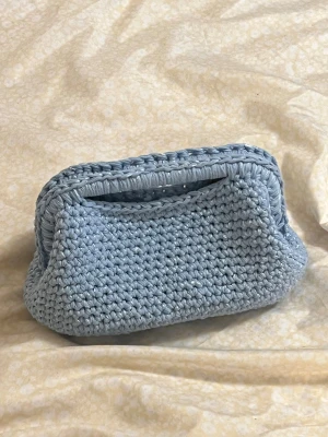 Ljusblå virkad kuvertväska - Handvirkad Clutch bag i 100% bomull med glittriga paljett detaljer. Passar både för vardagen men också till en festlig look. Längd: 17,5 cm Bredd: 15 cm Djup: 16,5 cm 