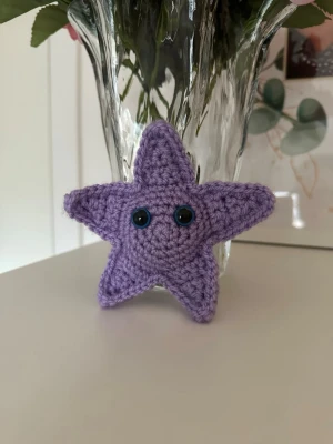 Virkad lila stjärna - Söt handvirkad liten stjärna i lila akrylgarn med blå ögon. Ca 12 cm i diameter. Den har säkerhetsögon som inte rekommenderas för barn under 3 år!💜⭐️