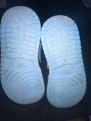 Jordan 1 Mid svart/blå sneakers - Snygga Air Jordan 1 Mid sneakers i svart och blått med klassisk Jumpman-logga på plösen. Skorna har svarta skosnören, perforerad tåbox och vit sula. Tillverkade i läder och textil för en stilren look.