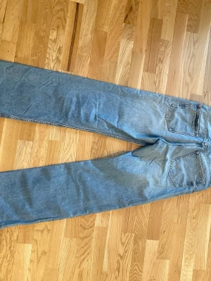 Blå raka jeans i klassisk modell - Säljer ett par blå jeans med rak passform och mid waist. Jeansen har två bakfickor och är gjorda i ett klassiskt denimtyg. Perfekta för en avslappnad och tidlös stil.