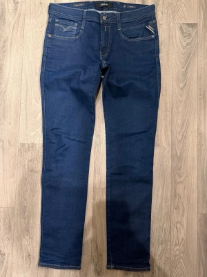 Replay Anbass Hyperflex Dry Mörkblå Jeans W33/L32 Slim Fit - Replay Anbass Hyperflex Dry mörkblå jeans i stretchigt och bekvämt material, slim fit modell som sitter bra och funkar till allt, storlek W33/L32, midja 42,5 cm, ytterbenslängd 104,5 cm, benöppning 16 cm, modellen är 185cm & väger 65kg, i fint skick.