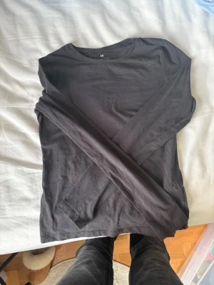 Svart långärmad topp från H&M - En enkel och stilren svart långärmad topp från H&M. Tillverkad i mjuk bomull med rund halsringning och normal passform. Perfekt att matcha med jeans eller kjol för en clean look.