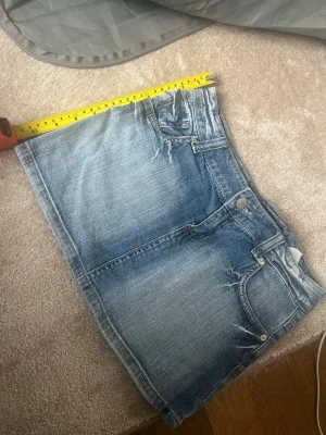 Blå jeanskjol från Tally Weijl - Säljer en snygg blå jeanskjol från Tally Weijl med klassisk femficksdesign och slitna detaljer. Kjolen har knapp- och dragkedjestängning framtill och är i en kort modell. Perfekt till sommaren och enkel att matcha med olika toppar.