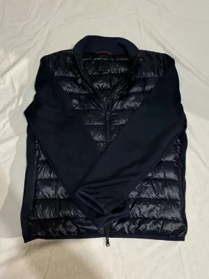 Mörkblå cardigan - Mörkblå cardigan med stickade ärmar och en glänsande front. Dubbelzip och en riktigt najs innerficka. Perfekt mot vår och sommar. Storlek M, sitter som S. Skriv vid minsta intresse 😀