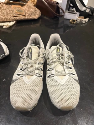 Nike vita mesh sneakers med grå detaljer - Snygga vita sneakers från Nike med grå swoosh och detaljer. Ovandelen är i ventilerande mesh och skorna har klassisk snörning. Perfekta för en sportig och stilren look. Lätta och bekväma att bära hela dagen.