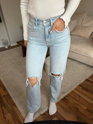 Ljusblåa jeans från Gina tricot  - Ljusblåa jeans med slitningar och hög midja från Gina Tricot. En liten fläck (inringad), syns bara på nära håll. Jag är 170cm för referens.