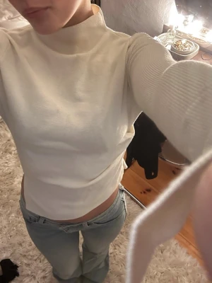 Vit ribbad polotröja med cut out - Trendig vit polotröja med ribbade detaljer och cut out på sidan. Tröjan har lång ärm och en tight passform. Perfekt till en utekväll eller till en middag!