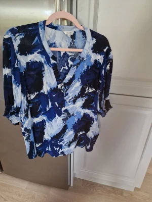 Blus från Cellbes - Snygg blus från Cellbes med abstrakt blått och vitt mönster. Blusen har v-ringning och trekvartsärmar.  Luftigt material som känns skönt mot huden.