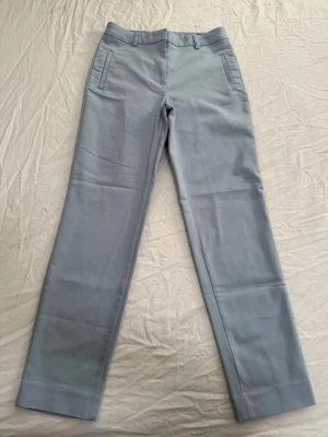 Ljusblå kostymbyxor med raka ben - Snygga ljusblå kostymbyxor med raka ben. Byxorna har två snedställda fickor fram, en bakficka och hällor för bälte.