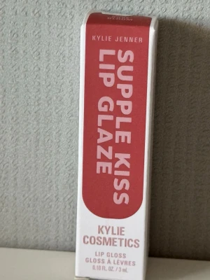 Kylie Cosmetics Supple Kiss Lip Glaze - Kylie Jenner Supple Kiss Lip Glaze är ett läppglans i en snygg rosa nyans. Kommer i en stilren vit och rosa förpackning. Innehåller oljor som solros, argan och kamomill för extra vård och glans. Perfekt för dig som vill ha mjuka och glansiga läppar.