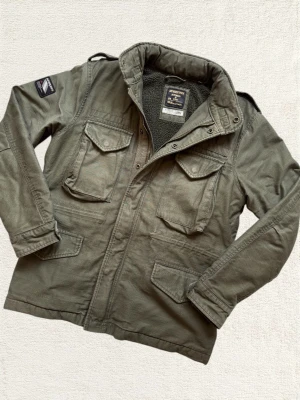 Superdry Fieldjacket - En mycket trevlig fieldjacket från Superdry i en fin ton av grön! Just denna påminner om den klassiska M65:an! Hör av dig vid frågor! 