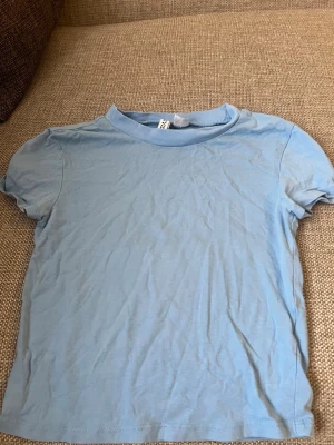 Ljusblå basic t-shirt från Chmpgn - En enkel och stilren ljusblå t-shirt T-shirten har korta ärmar, rund halsringning och är gjord i mjuk bomull. Perfekt till jeans eller shorts för en clean look. BARNSTORLEK !