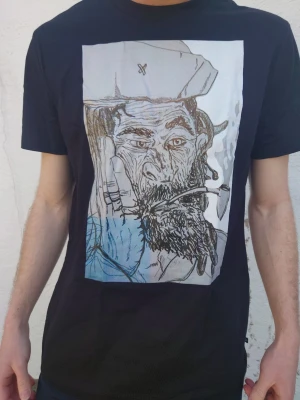 Svart t-shirt med konstnärligt tryck - Svart t-shirt med ett stort konstnärligt tryck på bröstet som föreställer ett porträtt i tecknad stil. T-shirten har rund hals och korta ärmar, perfekt för en avslappnad och cool look. Designad av mig kommer nytryckt vid köp. 👌I alla storlekar. DM vid intresse