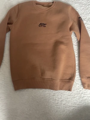 Beige Nike Air sweatshirt - Snygg beige sweatshirt från Nike Air med broderad logga på bröstet. Tröjan har rund halsringning, ribbade muddar och är tillverkad i mjukt material. Perfekt för en avslappnad och trendig stil.