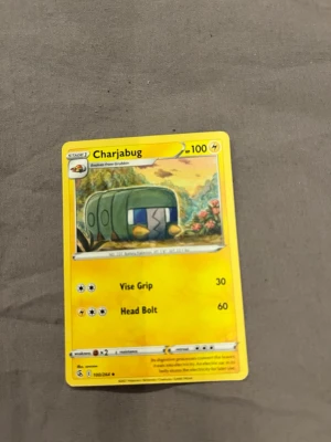 Pokémonkort Charjabug - Säljer ett Pokémonkort med Charjabug-motivet. Kortet har en gul ram och visar Charjabug i en tecknad naturmiljö. Energisymboler och attackerna Vise Grip och Head Bolt finns på kortet. Perfekt för samlare eller Pokémonfans.