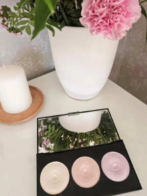 Revolution Highlight Palette trio - Highlight palette från Revolution med tre skimrande nyanser: en pärlvit, en champagne och en ljusrosa. Paletten har spegel i locket och rundade, pressade puder med vågmönster. Perfekt för att ge glow till ansiktet och framhäva dina drag. 🌸