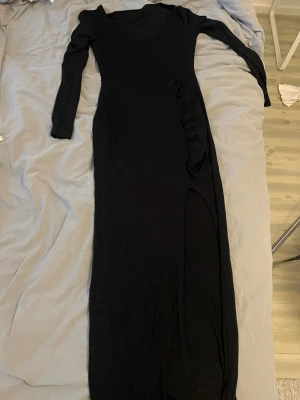 Svart långklänning med v-ringning - Snygg svart långklänning med v-ringning och långa ärmar. Klänningen har en figurnära passform och är tillverkad i ett mjukt material som ger en elegant siluett. Perfekt för dig som gillar stilrena och klassiska plagg.